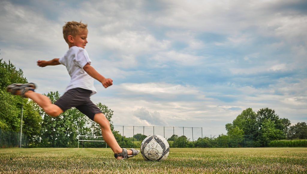 Junge spielt Fußball in Sandalen